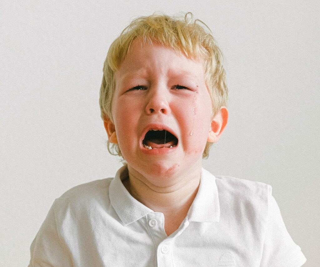 Picture of a crying boy with a white shirt in front of a white wall
